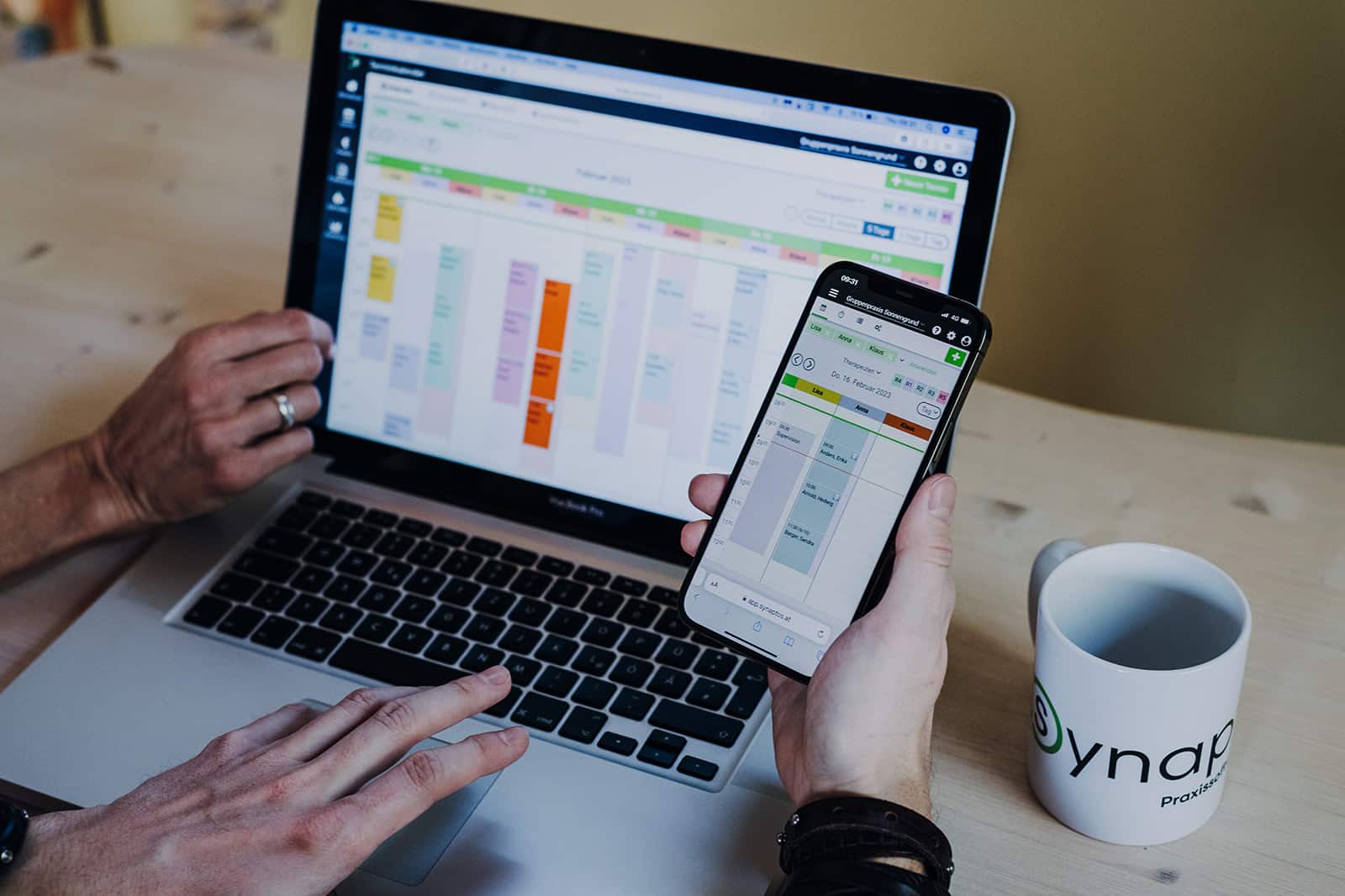 MacBook-Bildschirm und Smartphone-Bildschirm mit geöffnetem Praxiskalender von synaptos