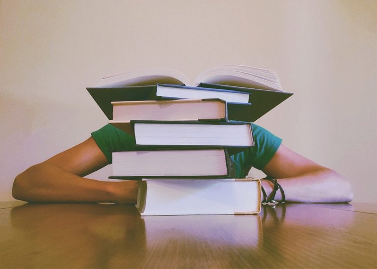 Stapel von Büchern auf einem Tisch vor Gesicht von Person