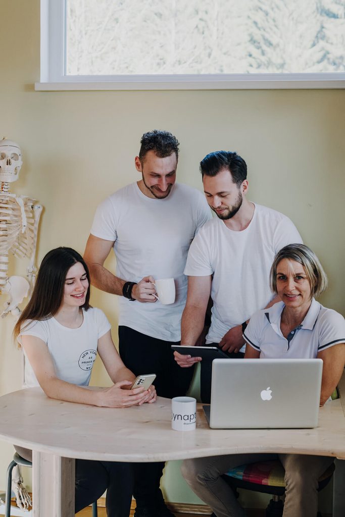 Zwei Männer und zwei Frauen in weißen T-Shirts mit Handy, Tablet, MacBook und Kaffetassen in Händen