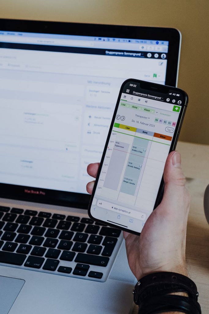 Mann hält Handy mit Praxiskalender in synaptos Applikation in rechter Hand