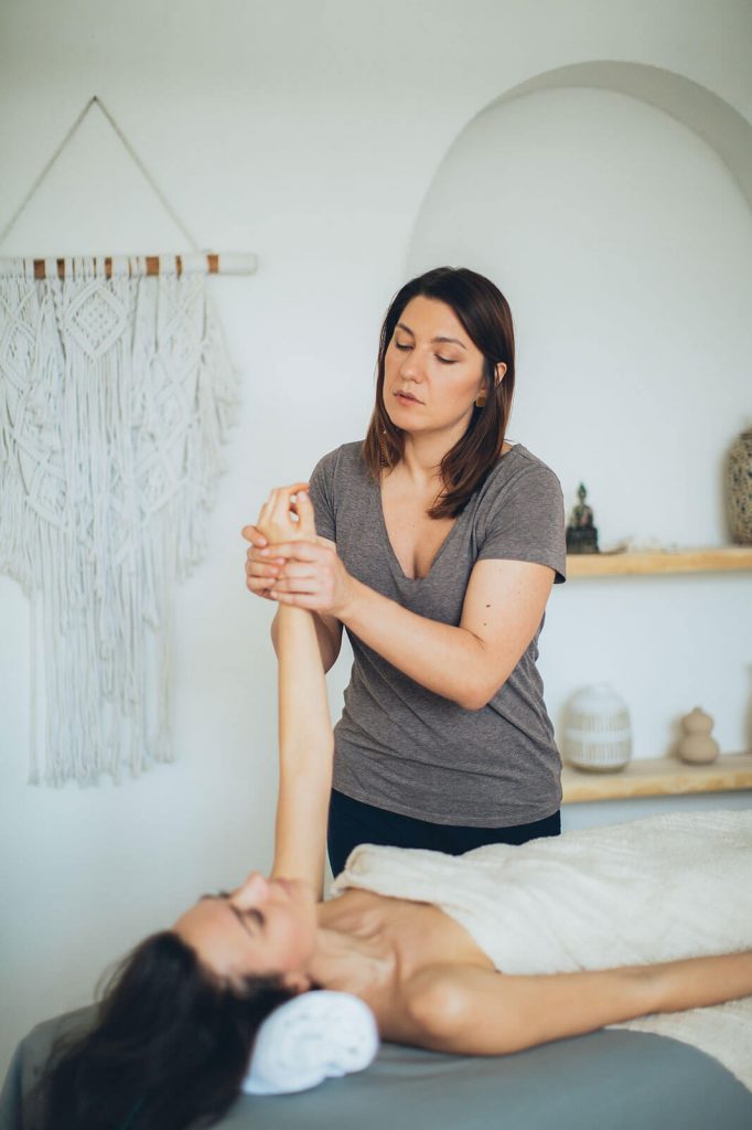 Masseurin massiert linkes Handgelenk von Patientin am nach oben gestreckten Arm