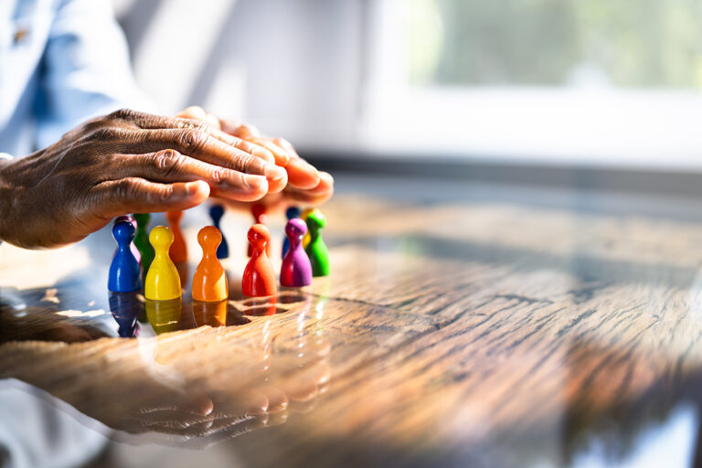 Mann hält schützende Hand über Spielfiguren in Regenbogenfarben